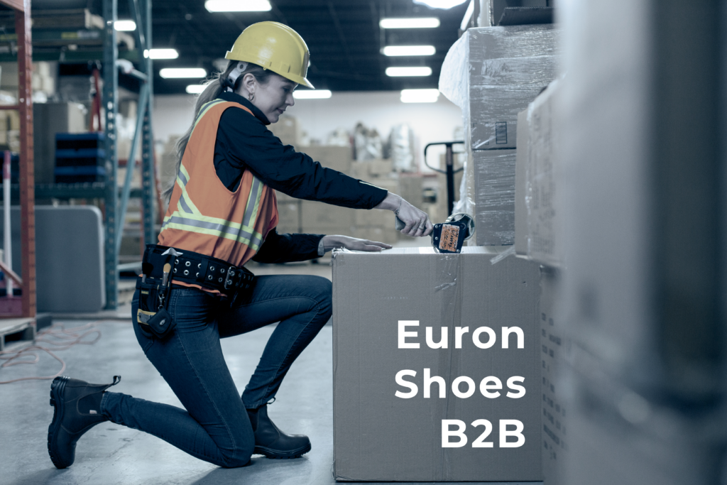 Euron warehouse worker kneeling while sealing a shipment box, wearing black safety Chelsea work boots